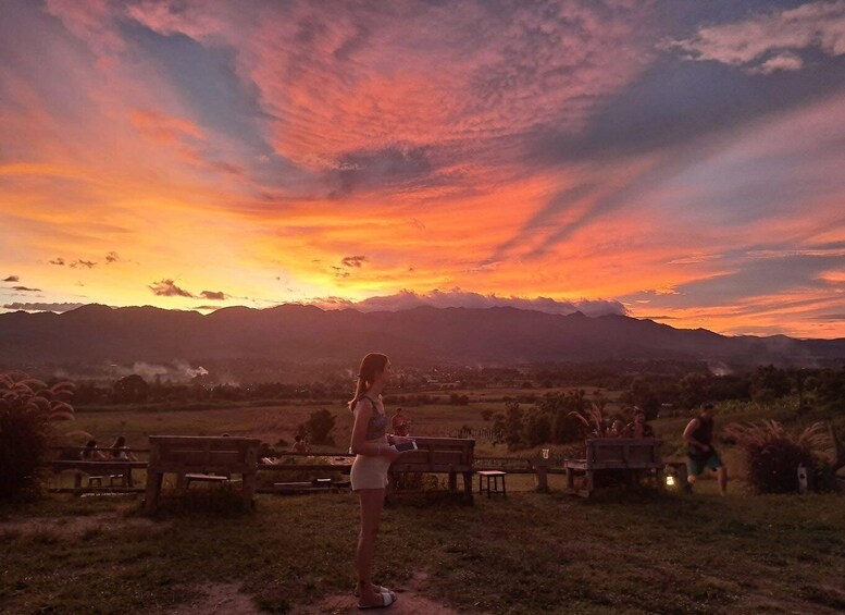 A sunset over a mountainous landscape with people sitting on benches. 3