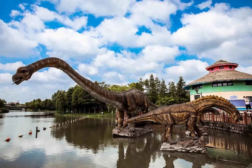 A dinosaur statue by a lake with a building in the background. 1