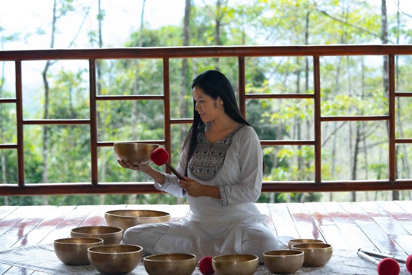 A person sitting on the floor surrounded by multiple bowls, likely engaged in meditation or a similar practice. 2