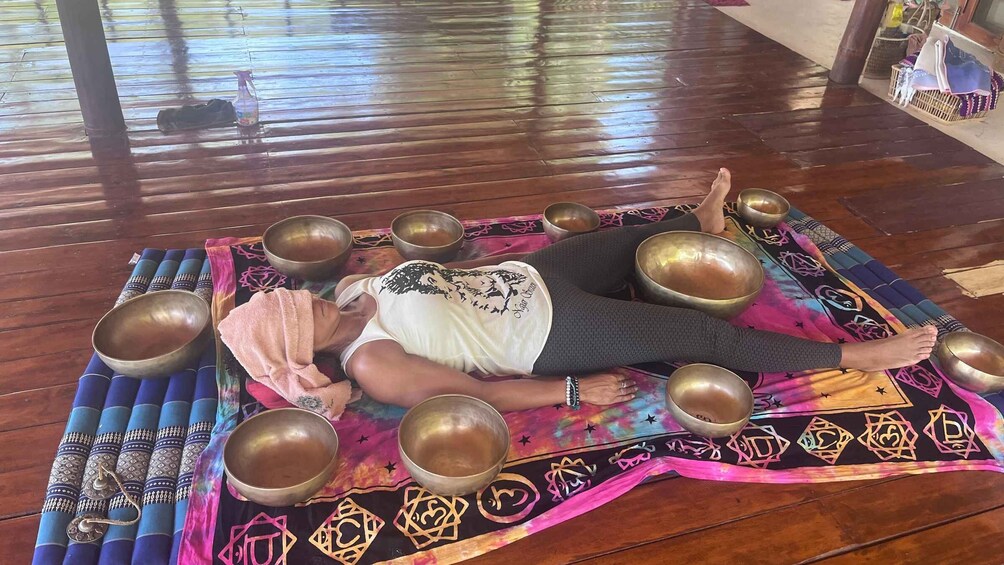 A person lying on a mat surrounded by several large bowls. 4