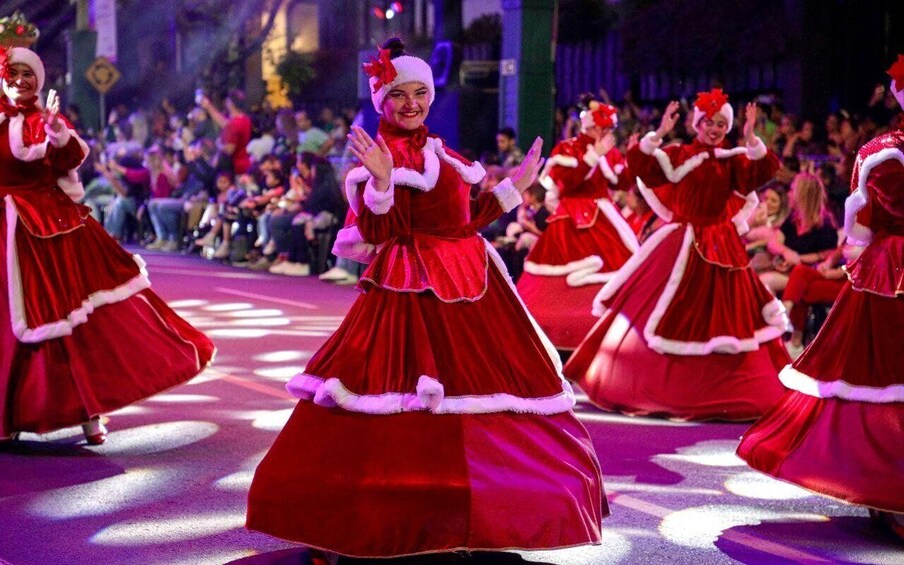 A group of performers in red dresses with white trim, dancing on a stage with an audience. 3
