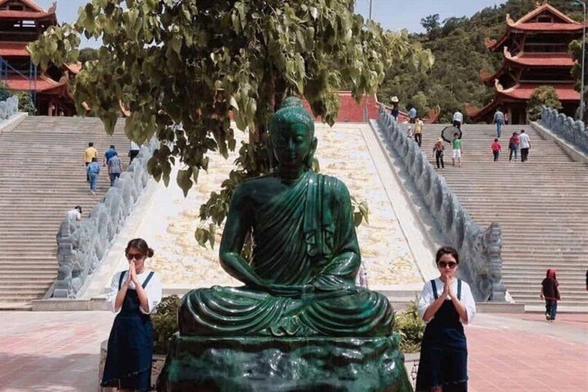 A large green Buddha statue with a tree in the background, surrounded by steps and people. 3