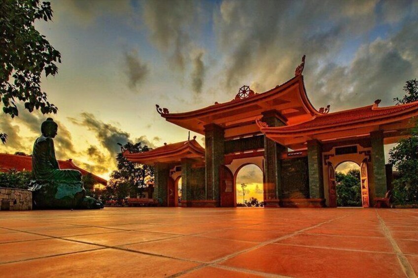 A traditional Chinese gate with a Buddha statue in front, set against a sunset sky. 5