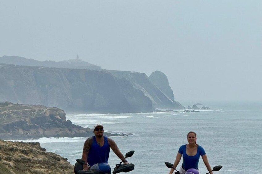 Two people on a beach with cliffs and a lighthouse in the background. 1