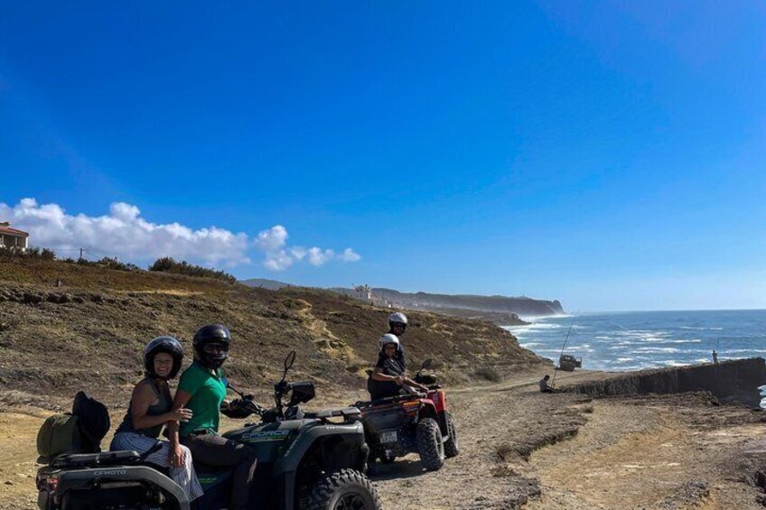 Three people on ATVs on a dirt path near the ocean. 4