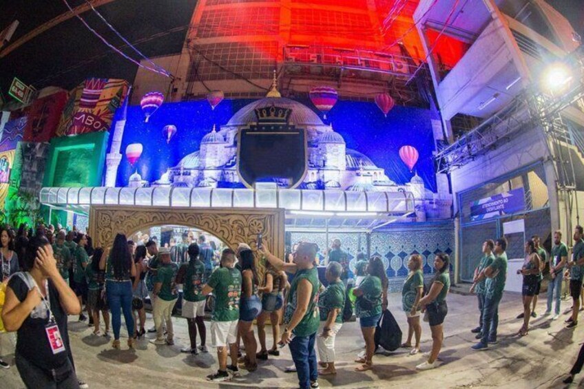 A crowd of people in green shirts gathered around a stage with a blue backdrop and a white structure. 3