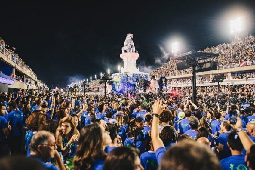 A large crowd at a nighttime event with a central statue illuminated by blue lights. 5