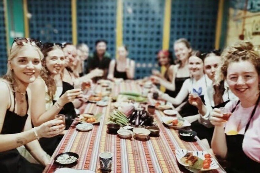 A group of people seated around a long table with food and drinks. 1