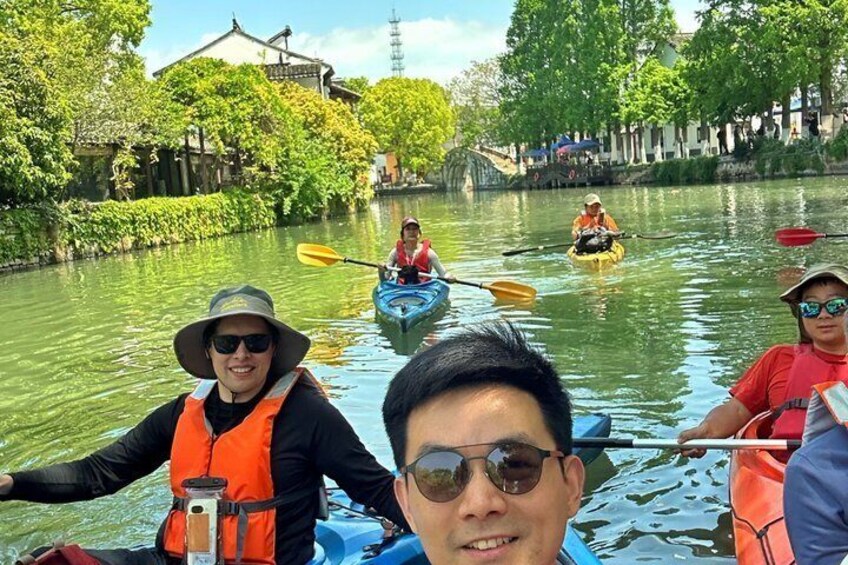 People kayaking on a river with traditional buildings in the background. 1