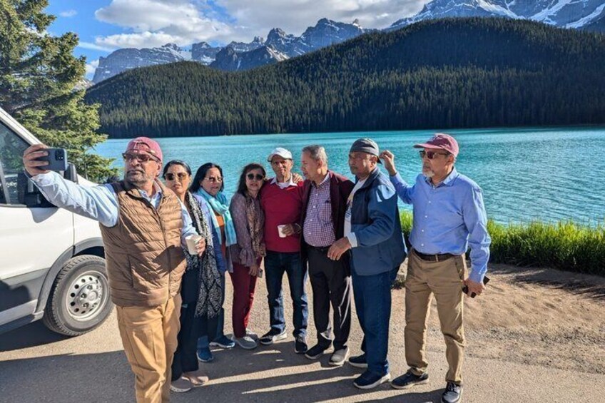 A group of people taking a selfie by a lake with mountains in the background. 2
