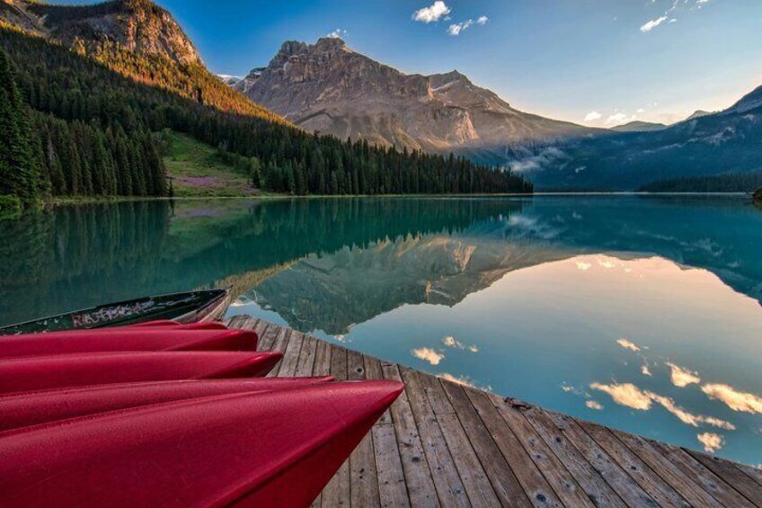A calm lake with reflections of mountains and a wooden dock with red canoes. 4