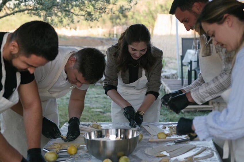 People preparing food outdoors, with lemons and a metal bowl on the table. 1