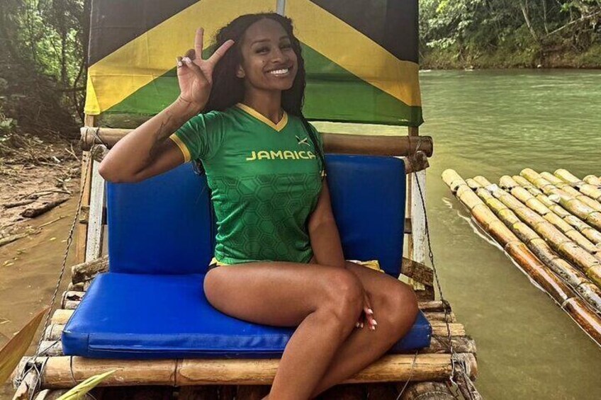A person sitting on a blue chair with a hammock, wearing a green shirt with 'JAMAICA' on it, and a flag in the background. 1