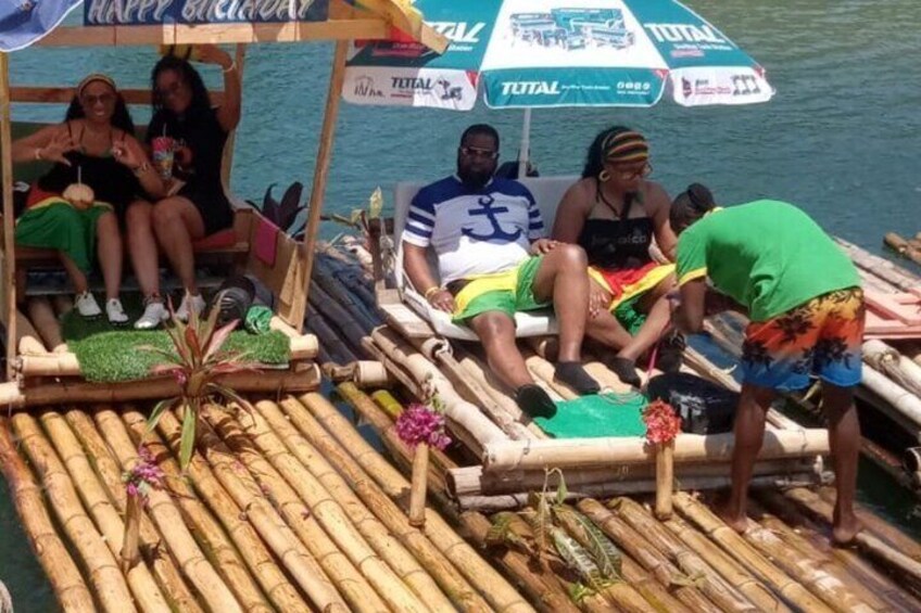 A bamboo boat with people sitting and a man standing, decorated with flowers and a 'Happy Birthday' sign. 5