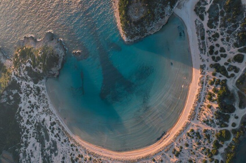 An aerial view of a coastal area with a sandy beach, clear turquoise waters, and rocky outcrops. 3