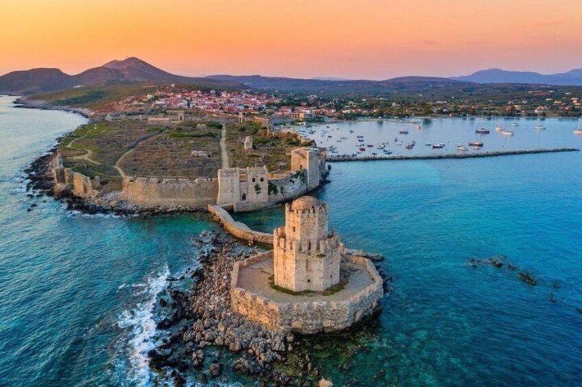 A coastal fortification with a prominent tower, surrounded by clear blue waters and a distant town. 1