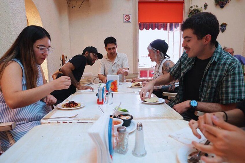 A group of people sitting around a table with food, engaged in conversation. 4