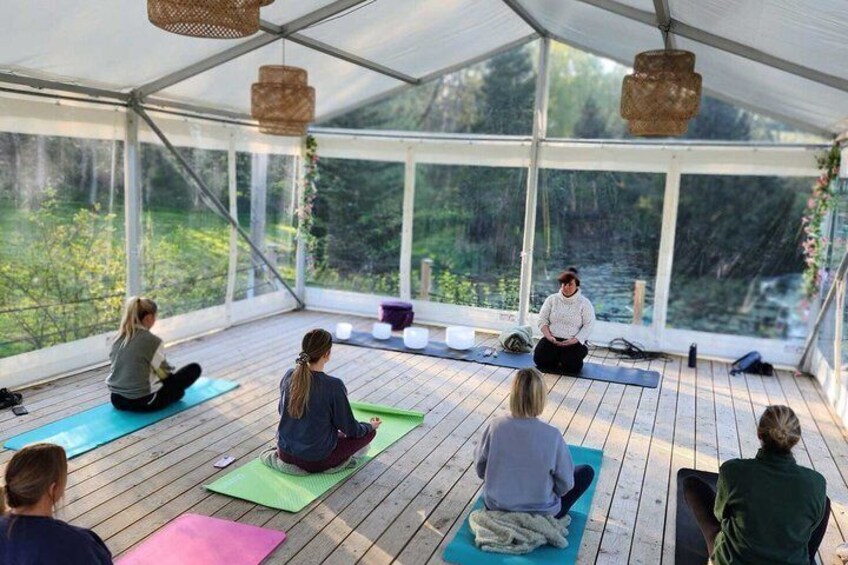A group of people sitting on yoga mats in a covered outdoor area with a view of greenery. 3