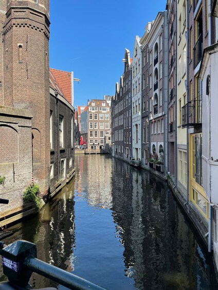 A canal with buildings on either side, a brick tower, and a clear blue sky. 4