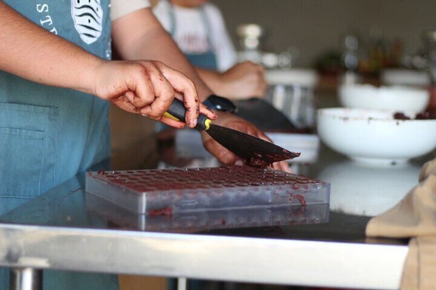 A person cutting a red substance on a metal surface in a kitchen setting. 1