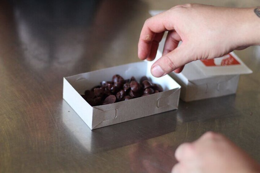 A hand reaching for a box of chocolate-covered candies on a wooden table. 5