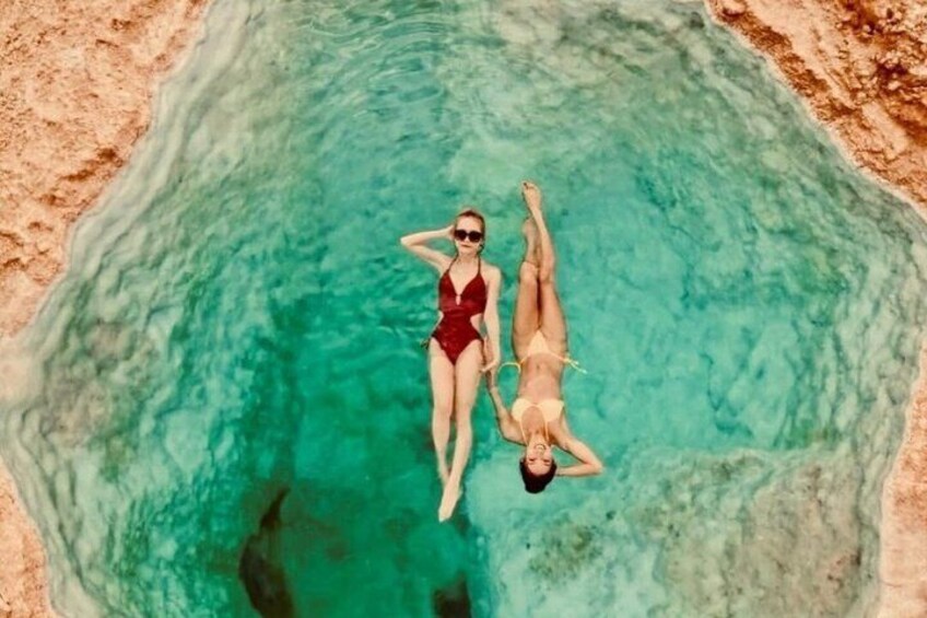 Two people floating in a clear blue pool surrounded by rocky terrain. 3