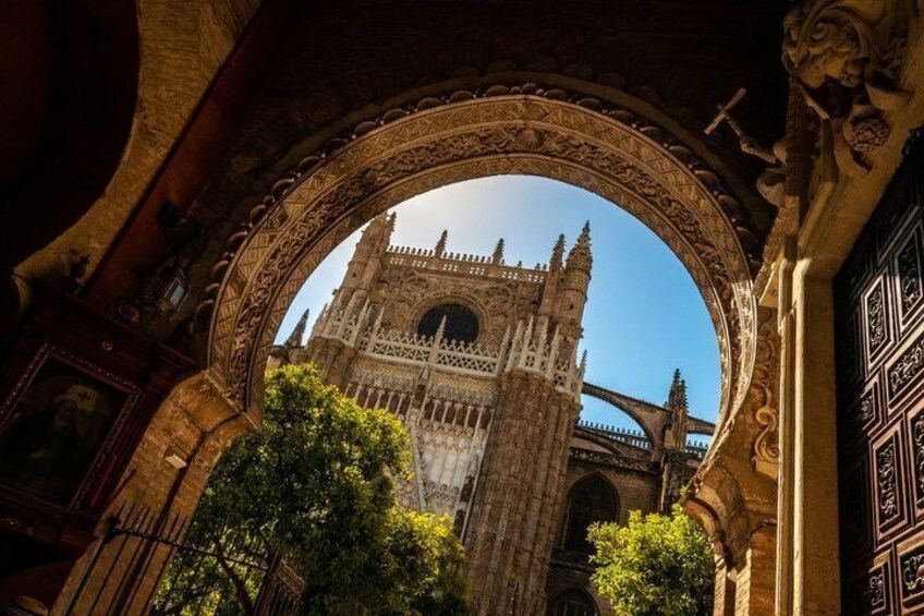 An ornate archway framing a historic cathedral with intricate carvings and a clear blue sky. 1
