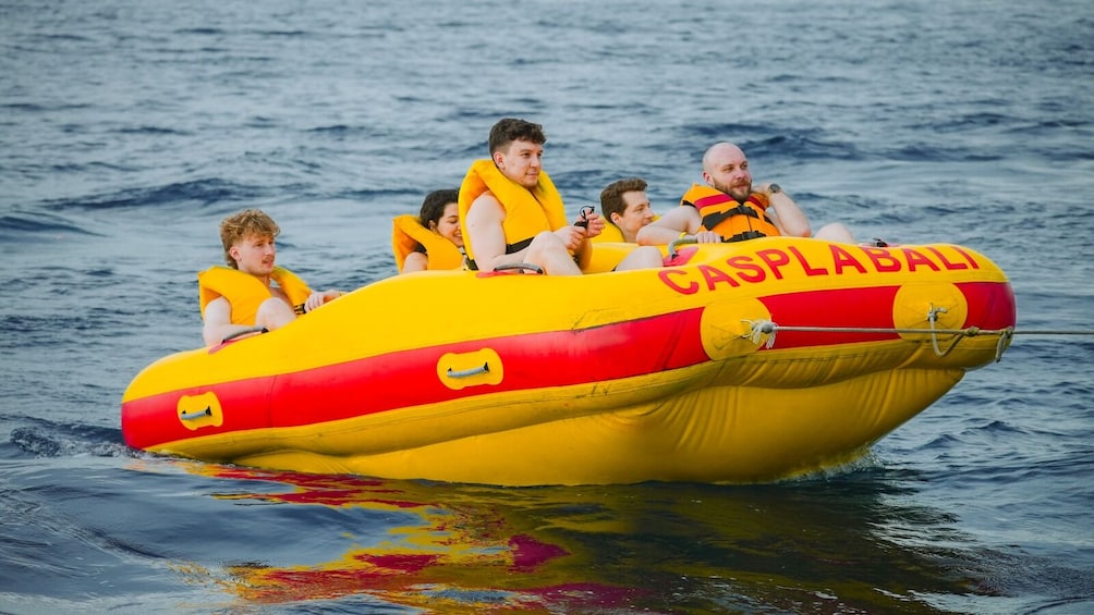 A group of people on a yellow and red inflatable boat with 'CASPLABALI' written on it, floating on water. 5