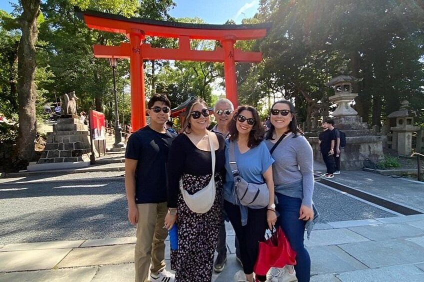 A group of people standing in front of a red torii gate with a stone monument and trees in the background. 5