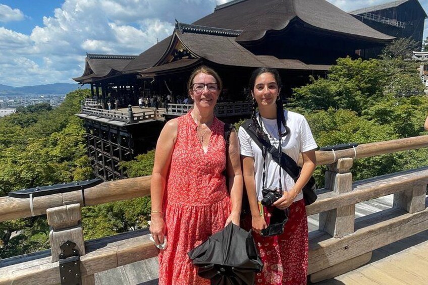 Two people standing on a wooden bridge with a traditional building in the background. 2