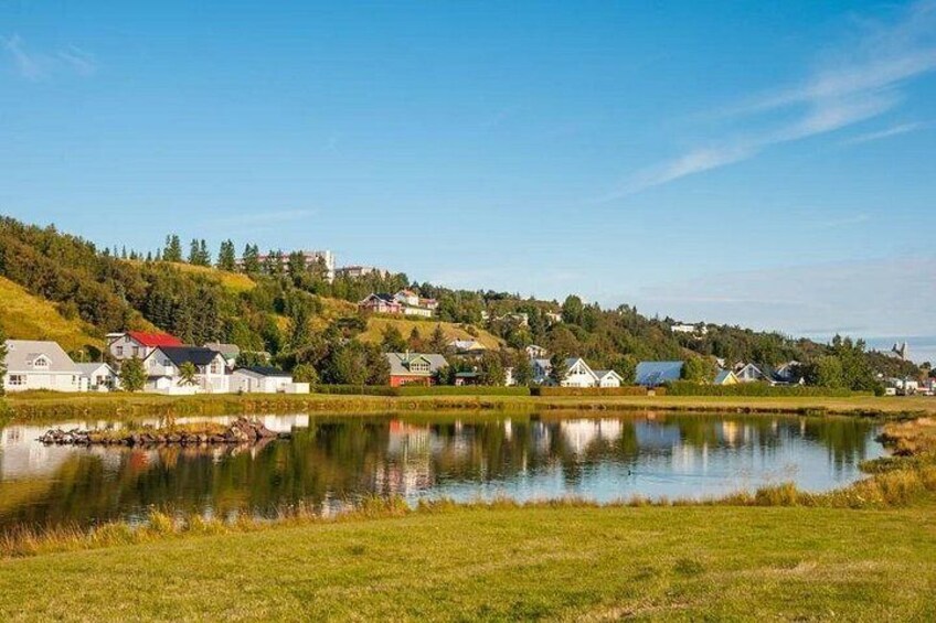 A calm lake with houses on the shore, a hill with trees, and a clear sky. 2