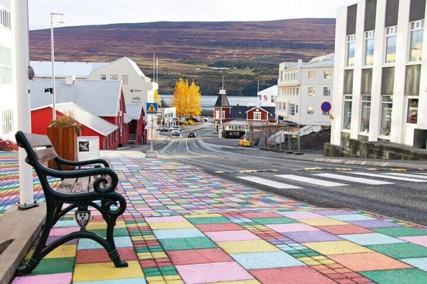 A colorful tiled pedestrian walkway with a bench, buildings, and a view of a hill in the background. 2