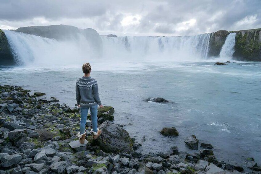 A person standing on rocks facing a waterfall. 1