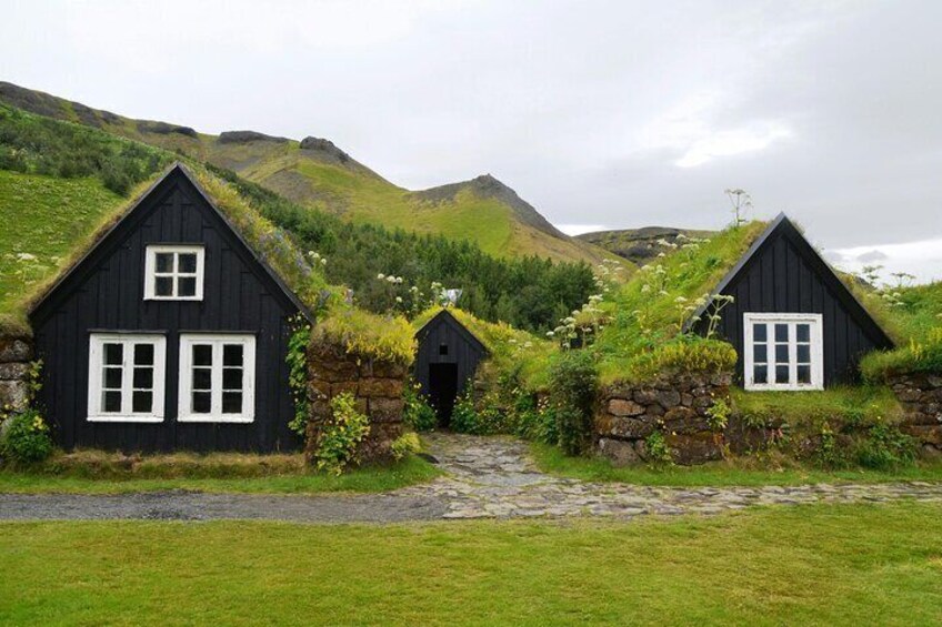 A row of black houses with white windows and stone walls, surrounded by green grass and hills. 5