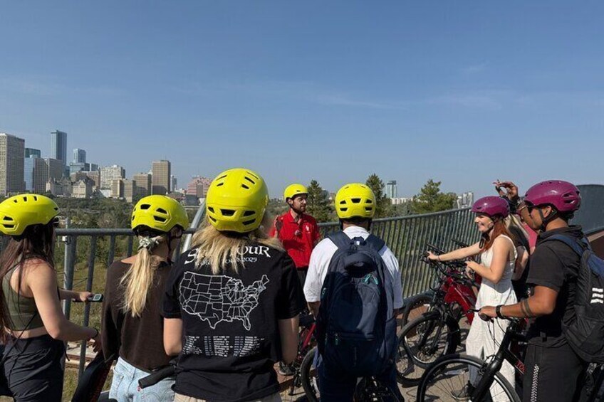 A group of people wearing helmets, standing on a bridge with a city skyline in the background. 5