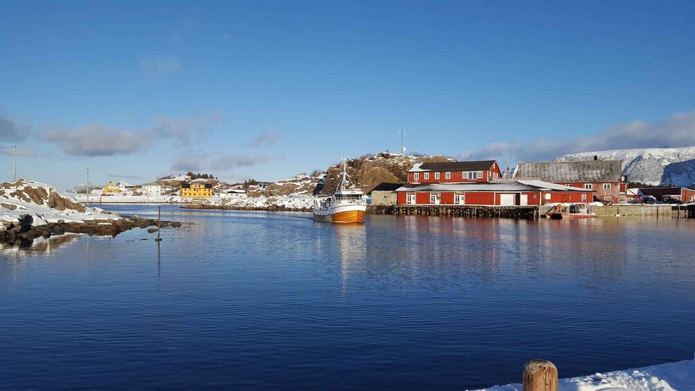 A calm harbor with a wooden boat, red buildings, and snow-covered hills. 2