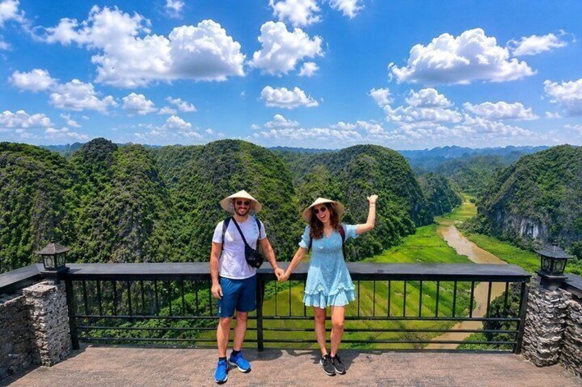 Two people standing on a bridge with a river and forested hills in the background. 5