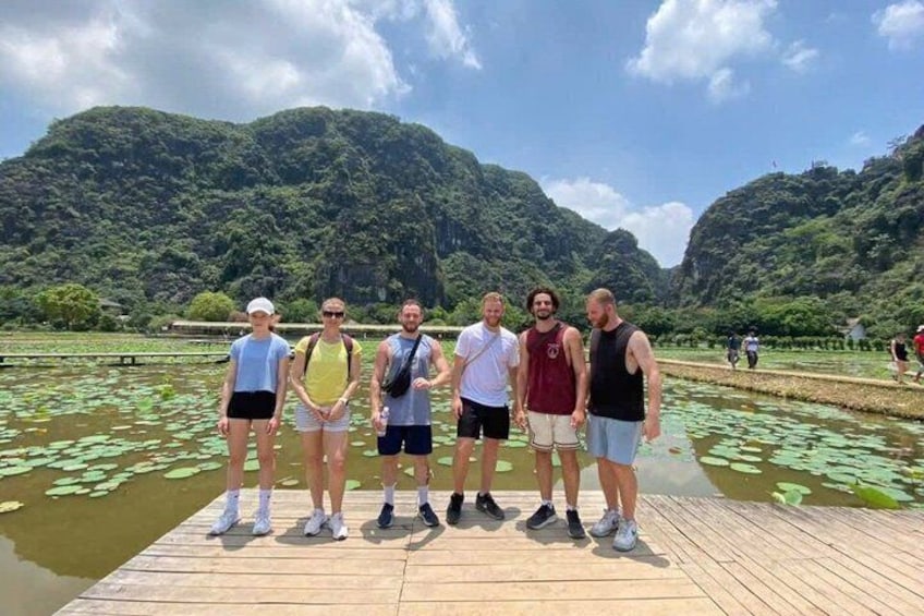 A group of people standing on a wooden dock by a lake with lily pads and mountains in the background. 3