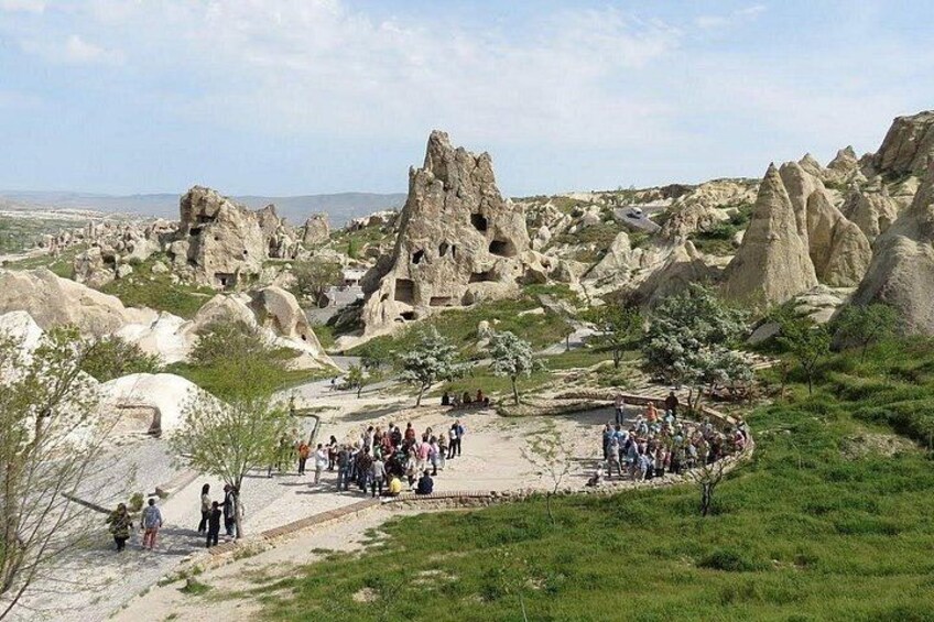 A rocky landscape with unique geological formations, a group of people gathered near a structure, and a clear sky. 2