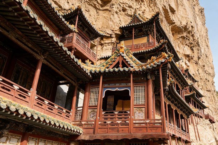 A traditional Chinese building with ornate wooden balconies and intricate roof designs, built into a cliffside. 1