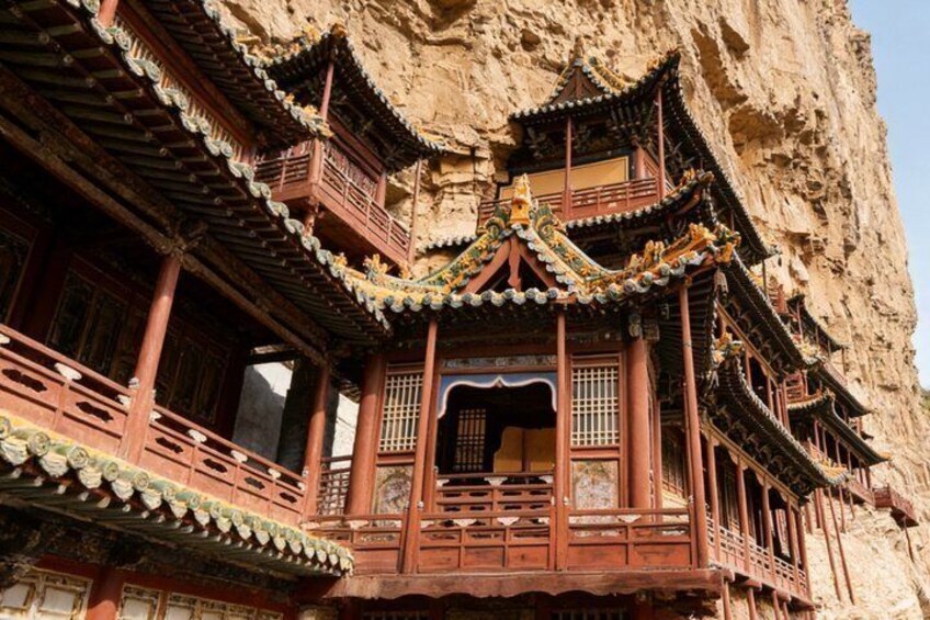 A traditional Chinese building with ornate wooden balconies and intricate roof designs, set against a rocky cliff backdrop. 1