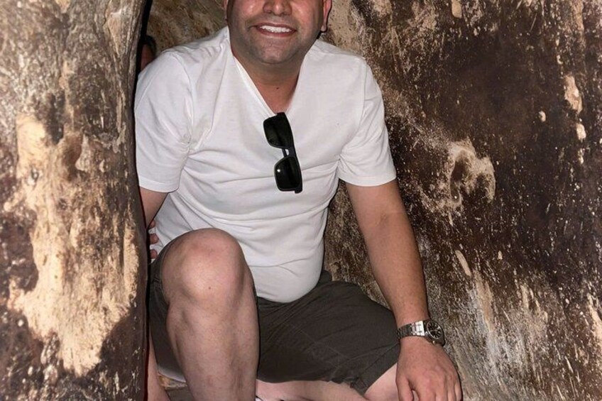 A person sitting in a cave with a white shirt and sunglasses hanging on the shirt. 2