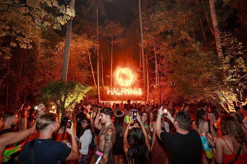A crowd at a nighttime outdoor event with a glowing circular sign in the background. 3