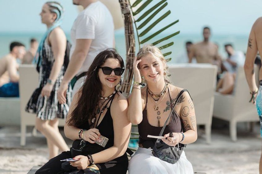 Two people sitting on a beach, one holding a drink and the other holding a phone. 2