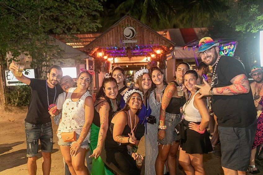 A group of people posing in front of a wooden structure with lights, surrounded by trees. 2