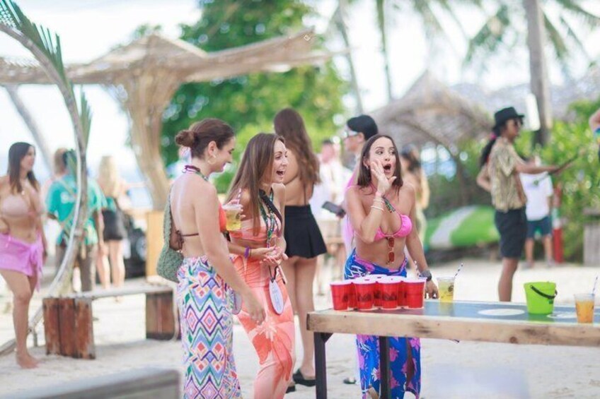 A group of people at a beach party with a table of drinks and tropical umbrellas. 4