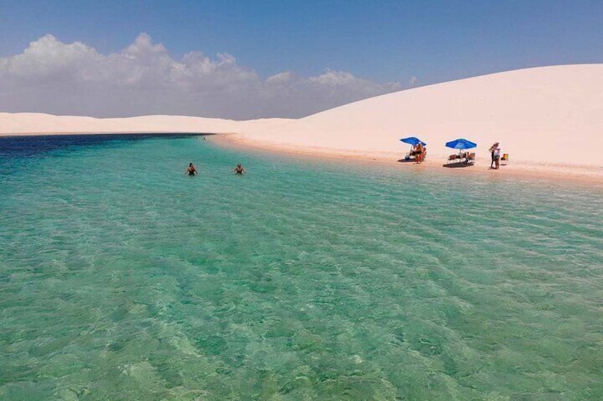 A beach with clear turquoise water, white sand, and a few people and umbrellas. 4
