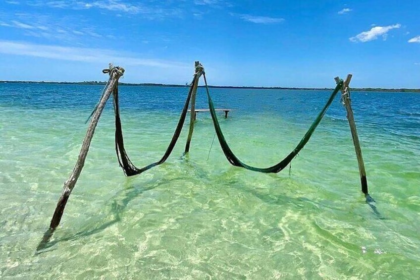 A hammock tied between two posts in clear shallow water. 2