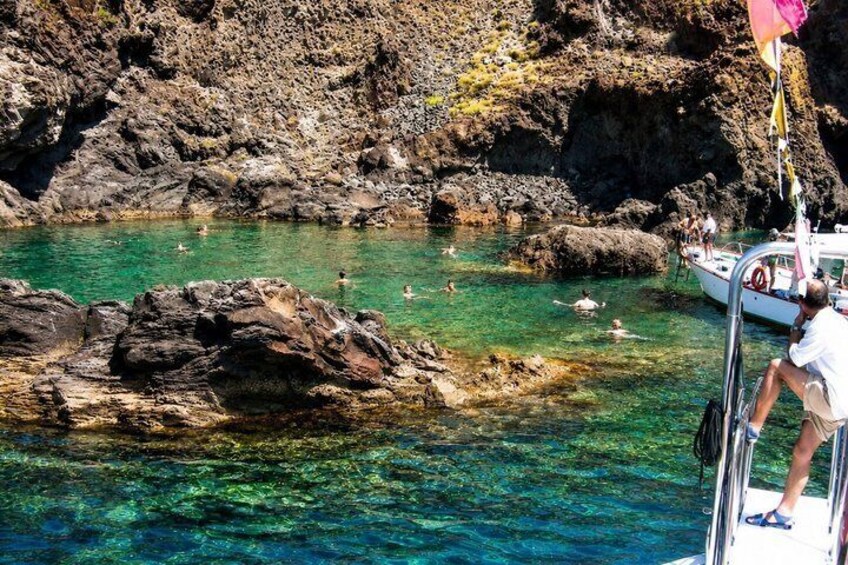 A rocky coastal area with clear turquoise water, a boat, and people swimming. 3