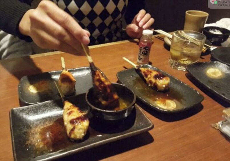 Skewers of grilled meat on a wooden table with a bottle of sauce and a glass of drink. 3